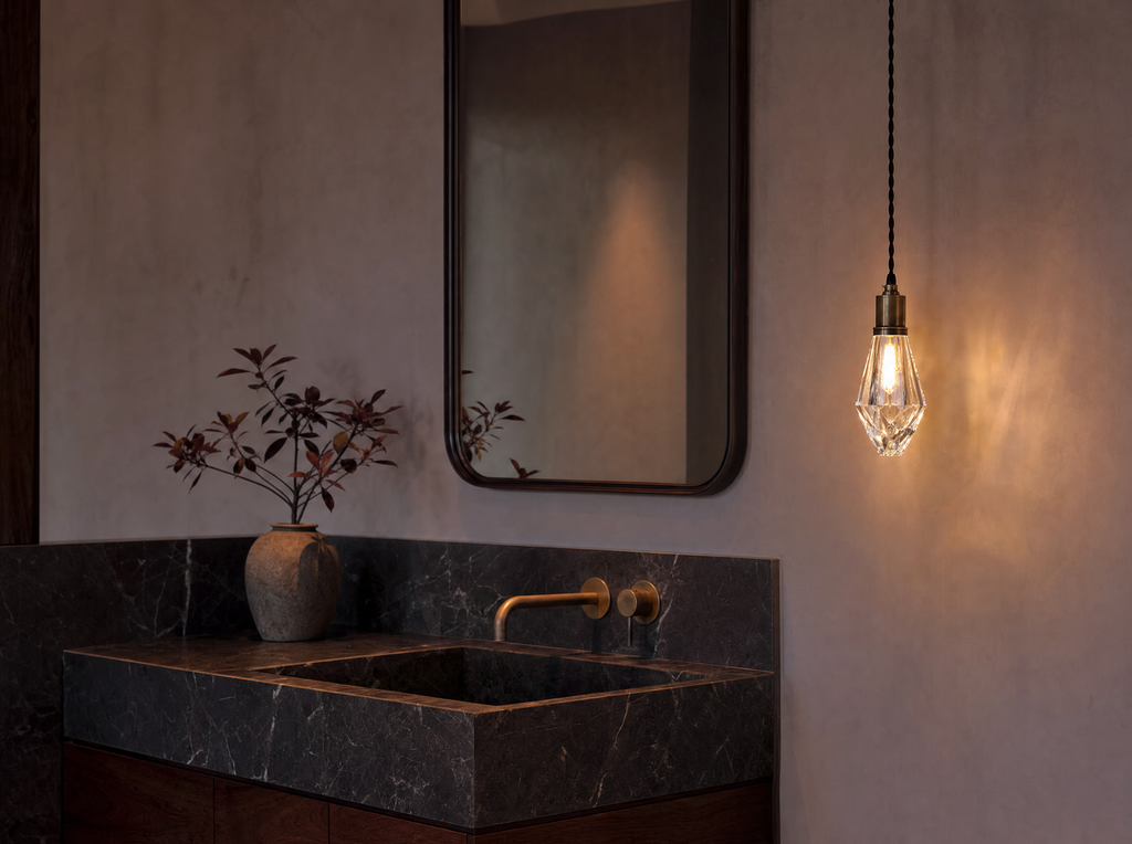 The single crystal pendant lit above a dark marble vanity