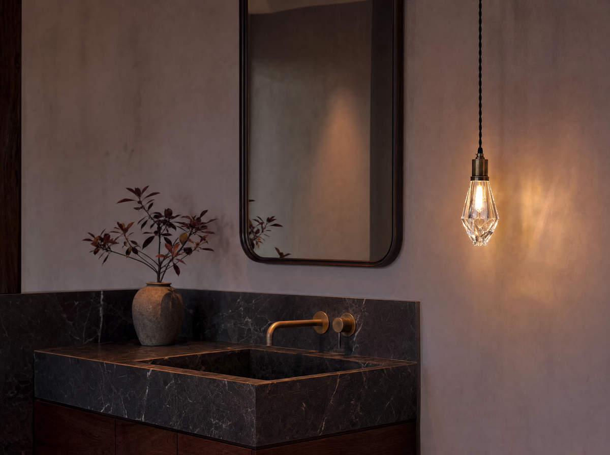 The single crystal pendant lit above a dark marble vanity